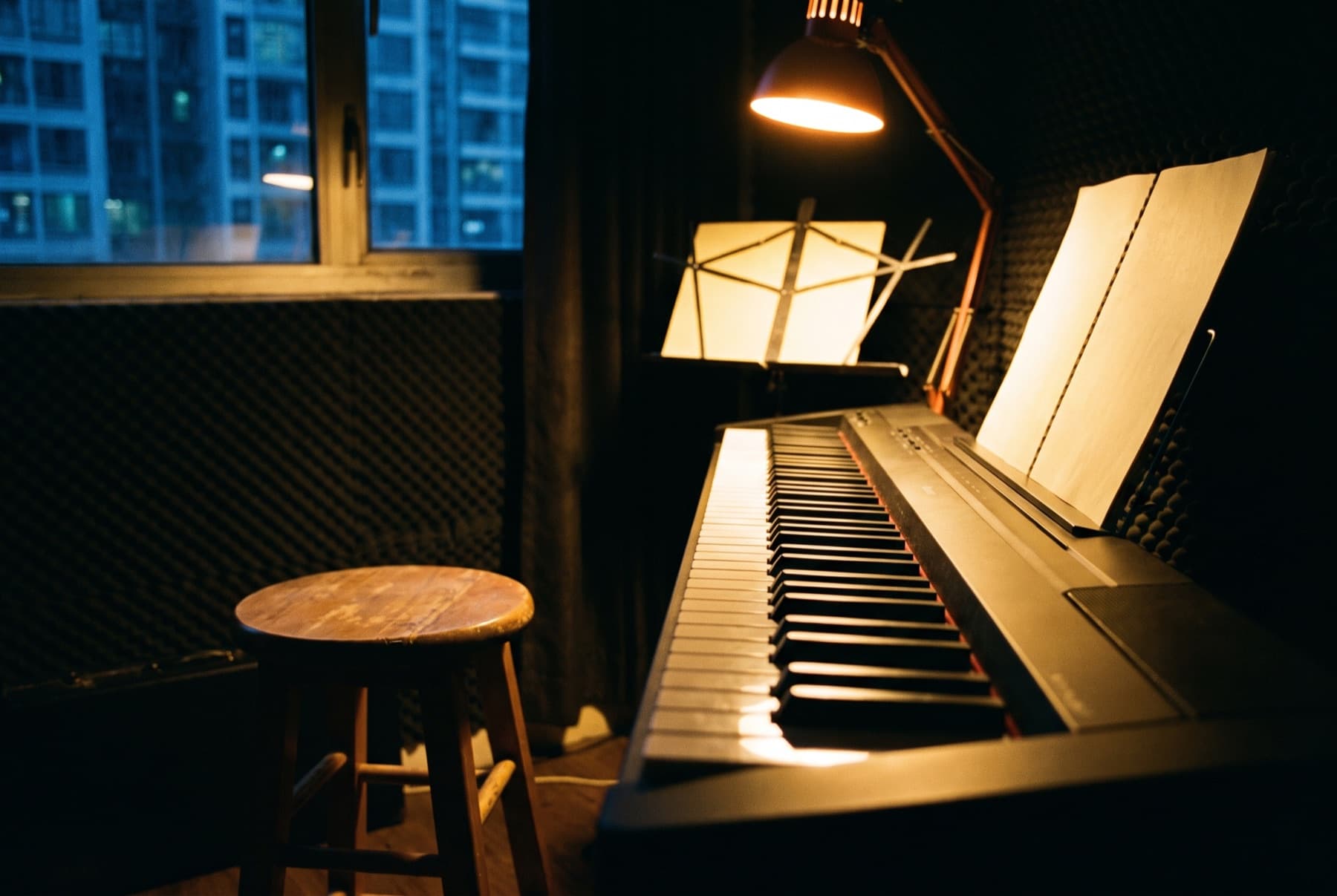Salle de travail éclairée à la lampe, un piano numérique ouvert au premier plan et un pupitre derrière